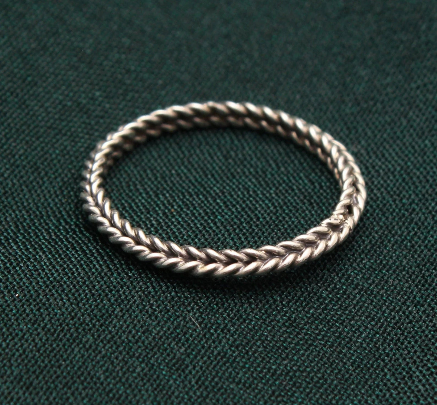 Sterling silver twisted braid band ring on dark green textured fabric background