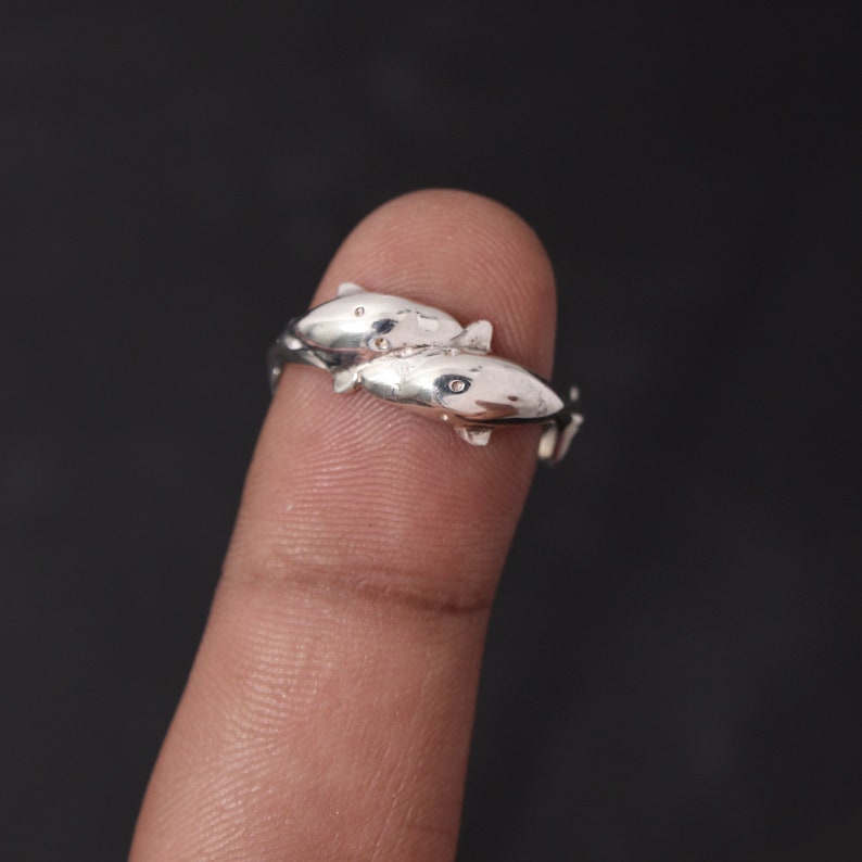Close-up photo of a sterling silver dolphin ring on a finger