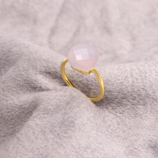 Gold-plated ring with faceted pale pink gemstone on soft gray fabric background
